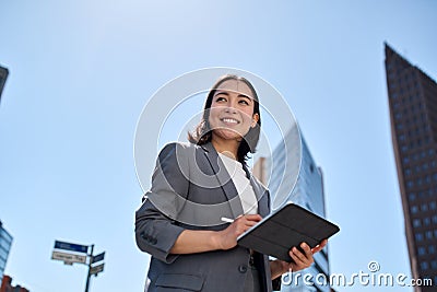 Smiling young Asian businesswoman using digital tablet on city street. Stock Photo