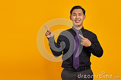 Smiling young Asian man pointing fingers at copy space on yellow background Stock Photo