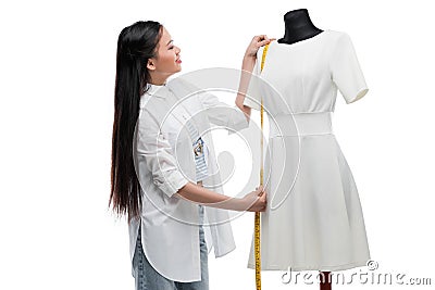 Smiling young asian tailor measuring stylish white dress on dummy Stock Photo