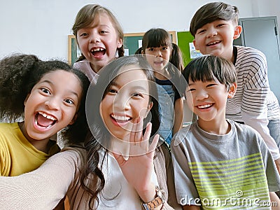 Smiling young Asian teacher making selfie with her schoolchildren in classroom. Elementary school,technology, children and people Stock Photo