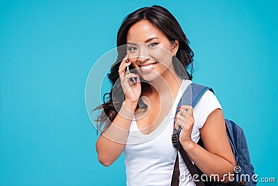 Smiling young asian woman with backpack talking on cellphone Stock Photo