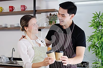 Smiling young barista couple loves Asian man and caucasian woman holding cups of hot coffee together. Start up Coffee shop and Stock Photo