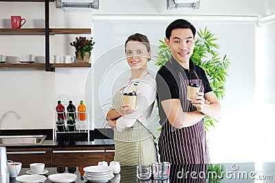 Smiling young barista and Waiters couple loves Asian man and caucasian woman holding cups of hot coffee together. Start up Coffee Stock Photo