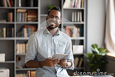 Smiling young biracial man in glasses holding digital computer tablet. Stock Photo