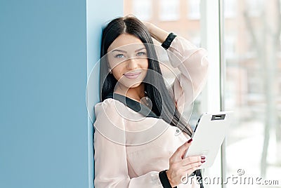 Smiling young business woman using tablet PC while standing relaxed near window at her office Stock Photo