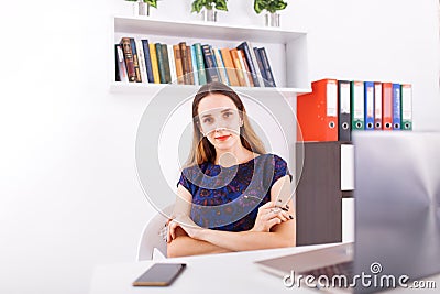 Smiling young businesswoman sitting at office desk working on a laptop, looking at camera Stock Photo