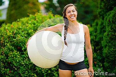 Smiling Young Expectant Mother Holding Exercise Ball In Park Stock Photo