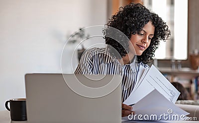 Smiling young female entrepreneur going over paperwork at home Stock Photo