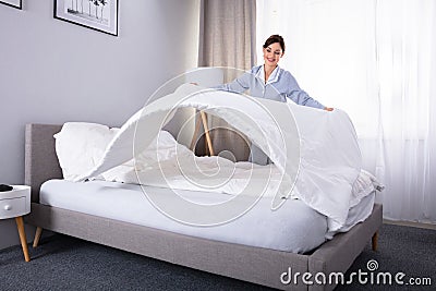 Housekeeper Arranging Bedsheet On Bed Stock Photo