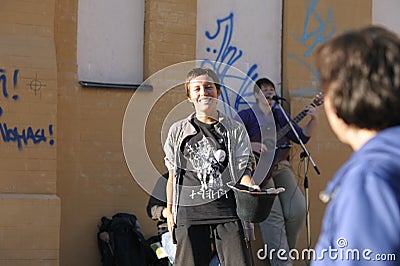 Smiling young girl holding a hat for collecting money, woman putting banknote into it, street musicians playing music on a Editorial Stock Photo