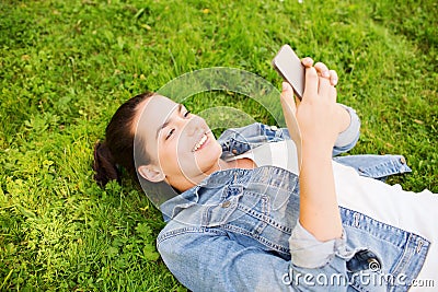 Smiling young girl with smartphone lying on grass Stock Photo
