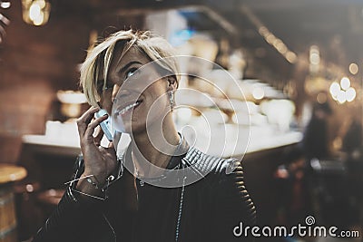 Smiling young girl using smartphone on background glow bokeh light in night atmospheric city.Hipster girl using in hands Stock Photo