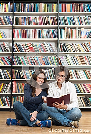 Smiling young girl and young man sitting on the floor in the lib Stock Photo