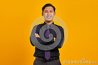 Smiling young handsome businessman crossing hands and look at camera on yellow background Stock Photo
