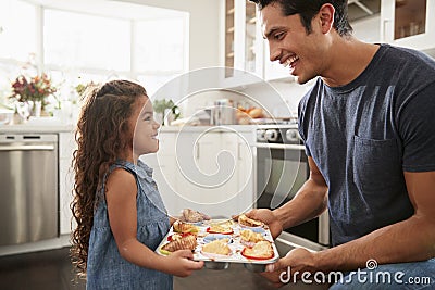 Smiling young Hispanic girl standing in kitchen presenting the cakes she has baked to her father Stock Photo