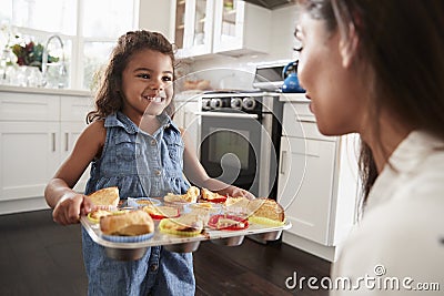 Smiling young Hispanic girl standing in kitchen presenting the cakes she has baked to her mother Stock Photo