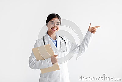 Smiling young indian lady in white coat with tablet shows finger at empty space, isolated on white background Stock Photo