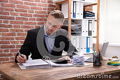 Male Accountant Calculating Invoice With Calculator In Office Stock Photo