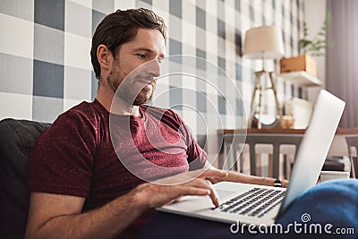 Smiling young man relaxing on his sofa using a laptop Stock Photo