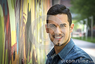 Smiling young man next to colorful graffiti wall Stock Photo