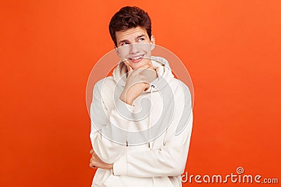 Smiling young man with peaceful face thinking over plans for future holding his chin, thoughtful teenager dreaming about good job Stock Photo