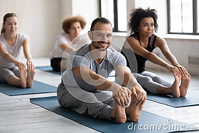 Smiling man practicing yoga at group lesson, Seated forward bend Stock Photo