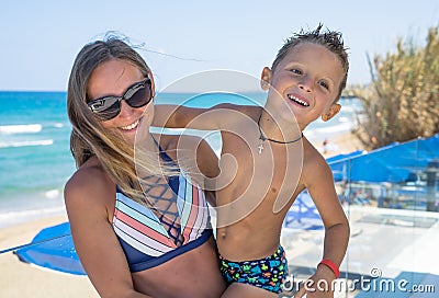 Smiling young mother kisses baby near the sea. Happy summer days. Stock Photo