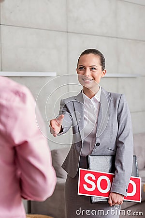 Smiling young saleswoman holding sold placard and document while greeting man in apartment Stock Photo
