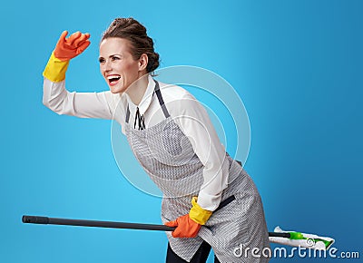 Smiling young scrubwoman using mop as broomstick on blue Stock Photo