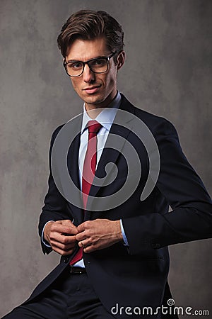 Smiling young seated businessman buttoning his suit Stock Photo