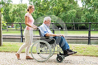 Smiling Young Woman Assisting Her Disabled Father On Wheelchair Stock Photo