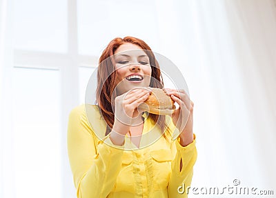 Smiling young woman eating hamburger at home Stock Photo
