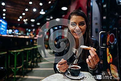 Smiling young woman eating traditional spanish churros with sugar dipped in hot chocolate sauce in a original spanish style cafe. Stock Photo