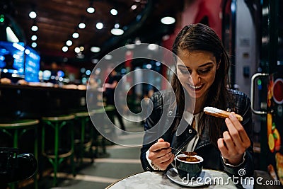 Smiling young woman eating traditional spanish churros with sugar dipped in hot chocolate sauce in a original spanish style cafe. Stock Photo