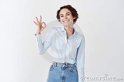 Smiling young woman feel assured, showing okay gesture in approval, praise good product, standing on white background Stock Photo