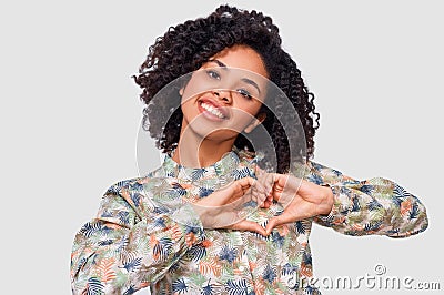 Smiling young woman making heart shape with fingers. Beautiful female with closed eyes, dressed in pink blouse, showing heart Stock Photo