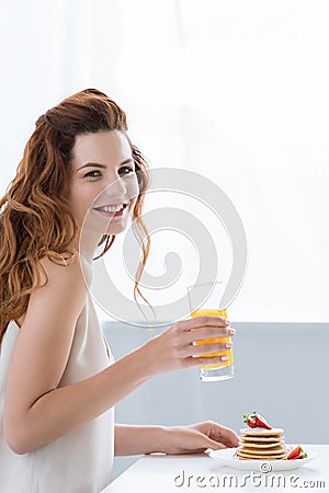 smiling young woman with orange juice and pancakes with strawberry for breakfast looking Stock Photo
