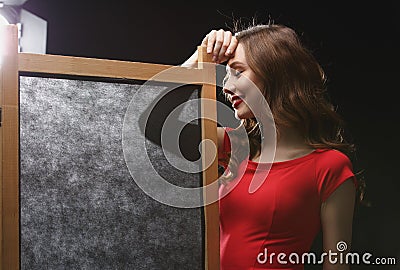 Smiling young woman in red dress standing near folding screen Stock Photo