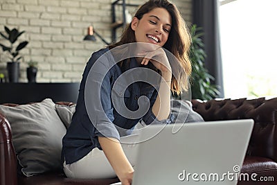 Smiling young woman sitting on sofa with laptop computer and chating with friends Stock Photo