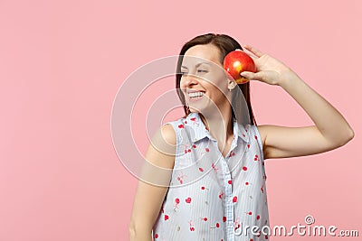 Smiling young woman in summer clothes looking aside holding fresh ripe red apple fruit isolated on pink pastel Stock Photo