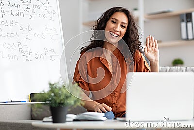 Smiling young woman teaching maths to students online, waving hello Stock Photo