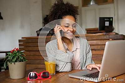 Smiling young woman using laptop and talking on mobile phone Stock Photo