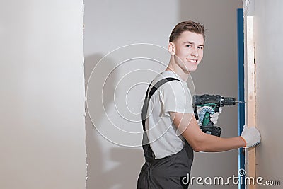 Smiling young working man in overalls drills screws with an electric screwdriver in an apartment Stock Photo