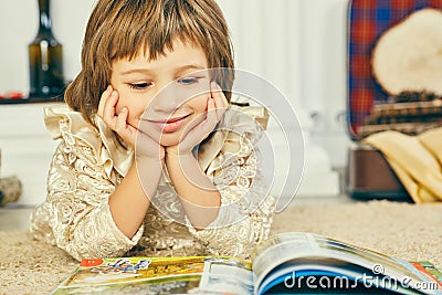 Smilling little Caucasian girl lying on the floor and reading an illustrated book. Stock Photo