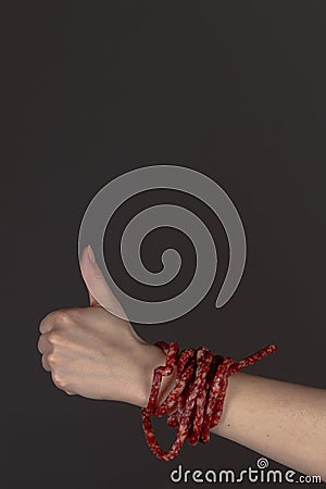 Smoked beer sausages are wrapped around the arm in the form of a bracelet and a like gesture is shown, thumbs up on a Stock Photo