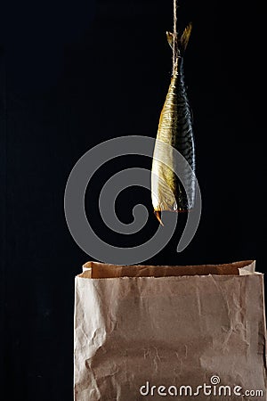 Smoked fish mackerel on the paper bag in the black wooden background Stock Photo