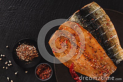 Smoked marinated mackerel fillets or fillet herring fish with spices, greens and slice of bread on plate over dark stone Stock Photo