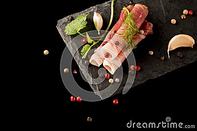 Smoked Parma Ham with Herbs, garlic and peppers on Stone Plate, composition on black background. top view, over lay Stock Photo