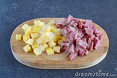 Smoked sausage and cheese cut in cubes on a wooden cutting board on a dark abstract background. Step by step cooking. Stock Photo