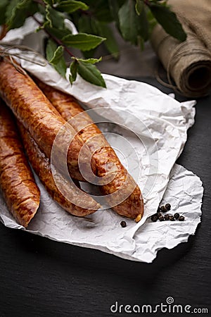 Smoked sausage in paper on a kitchen dark worktop. Stock Photo